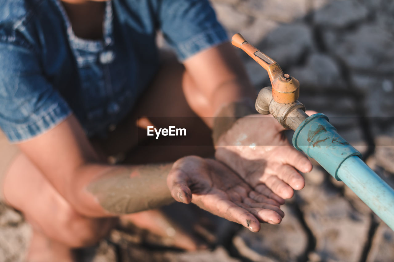 Boy with hands cupped crouching under empty faucet