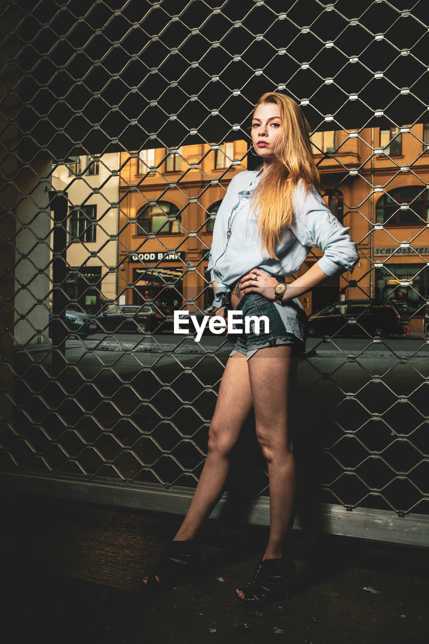 Portrait of woman standing against chainlink fence