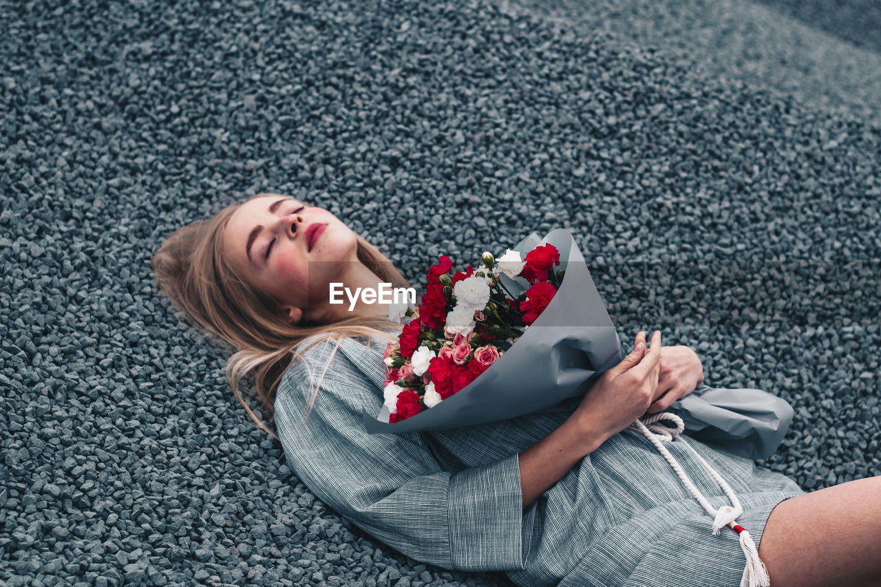 High angle view of woman with bouquet lying on gravels