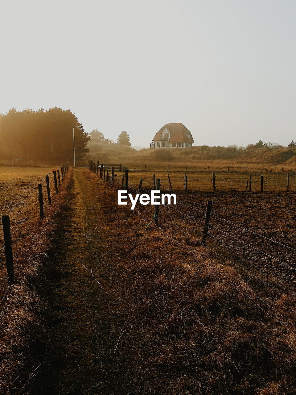 View of field separated by fence against clear sky