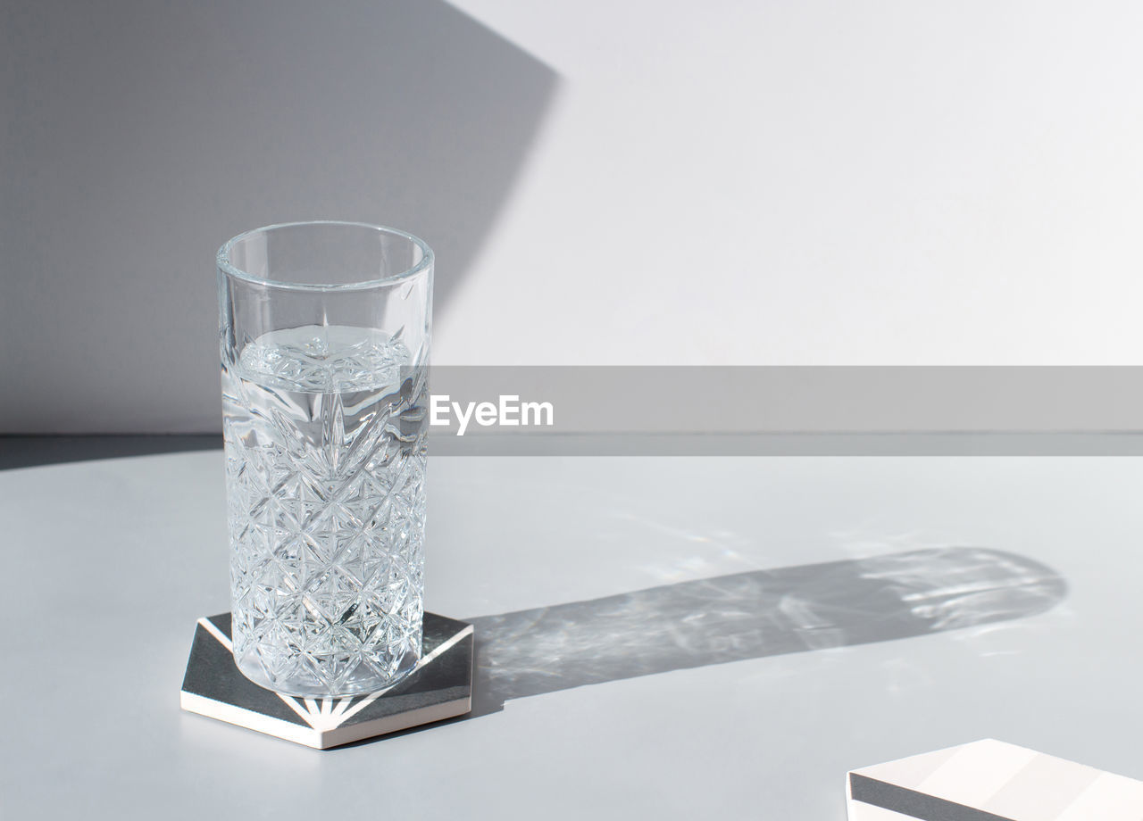 Faceted drinking glass of fresh clean water with shadow on grey table