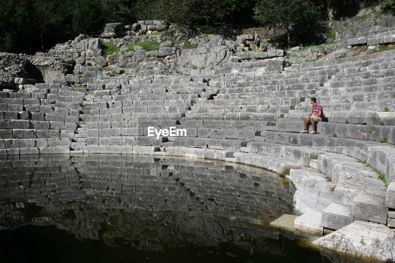 Man sitting on steps at pond