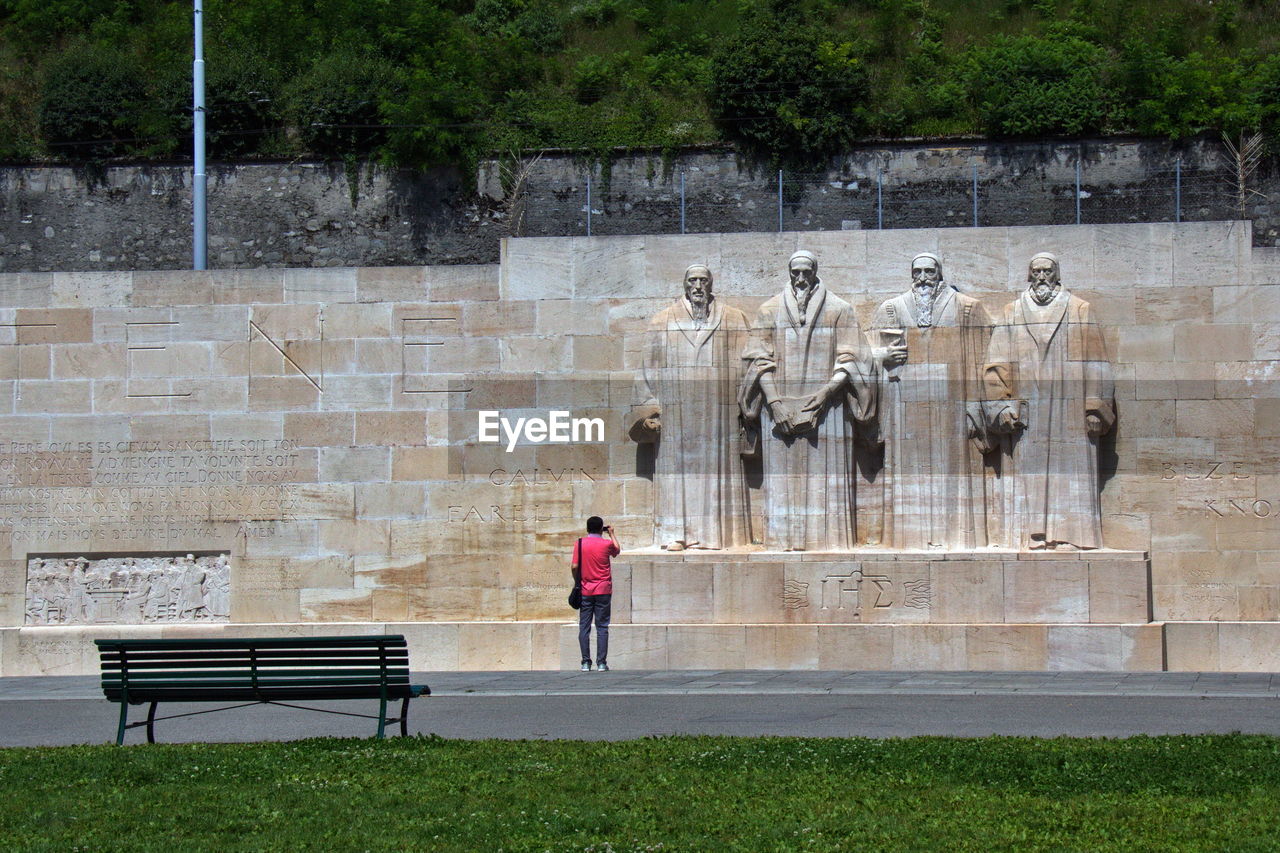 REAR VIEW OF MAN STANDING BY SCULPTURE