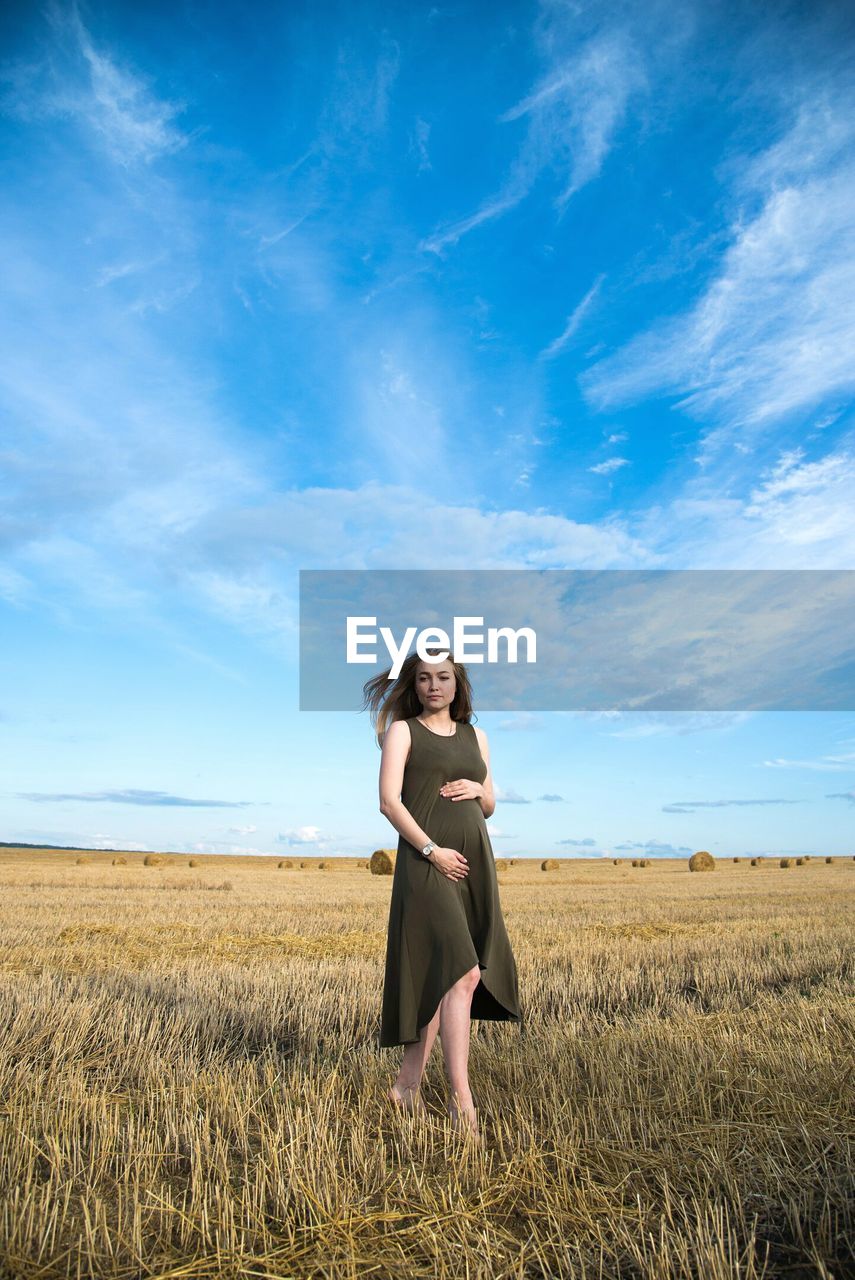 Pregnant woman standing on field against sky