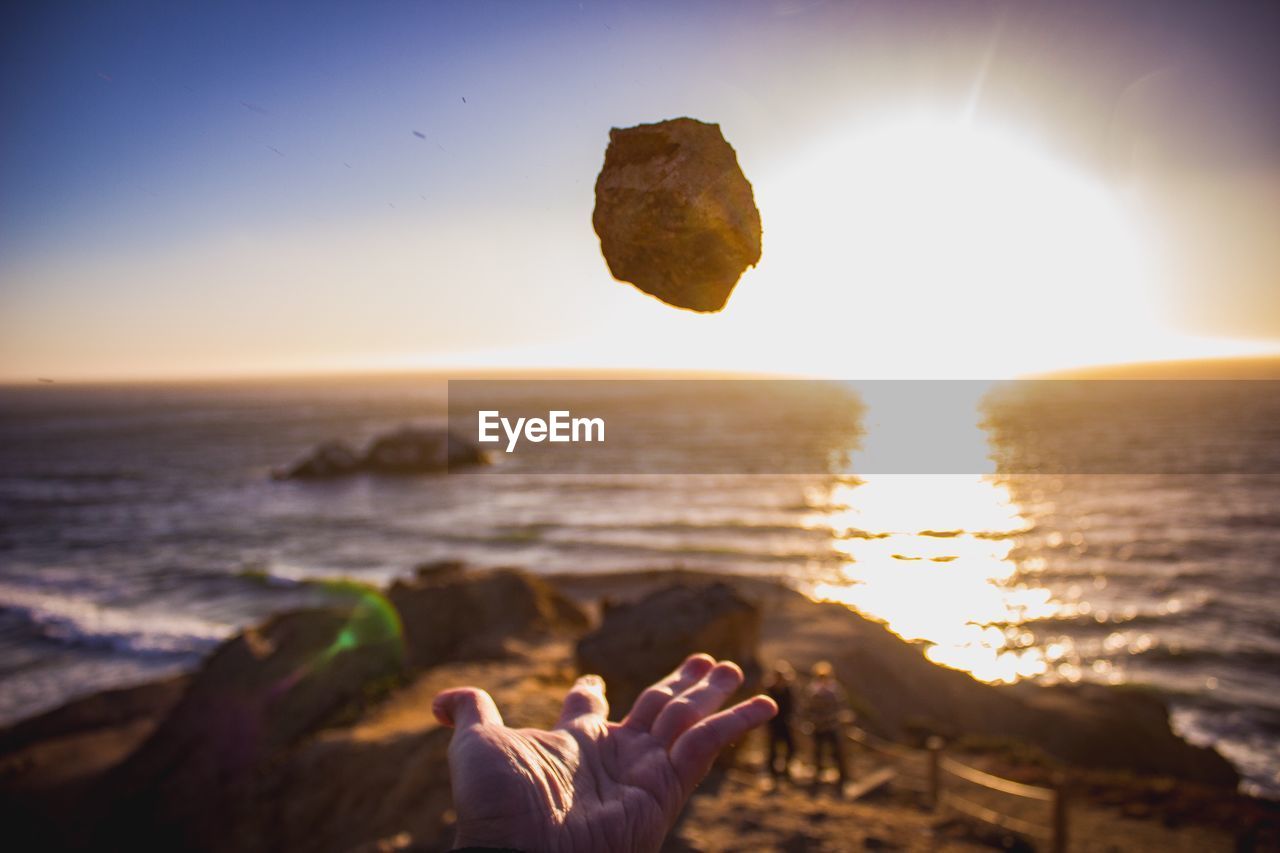 Close-up of person catching rock at beach against sky during sunset