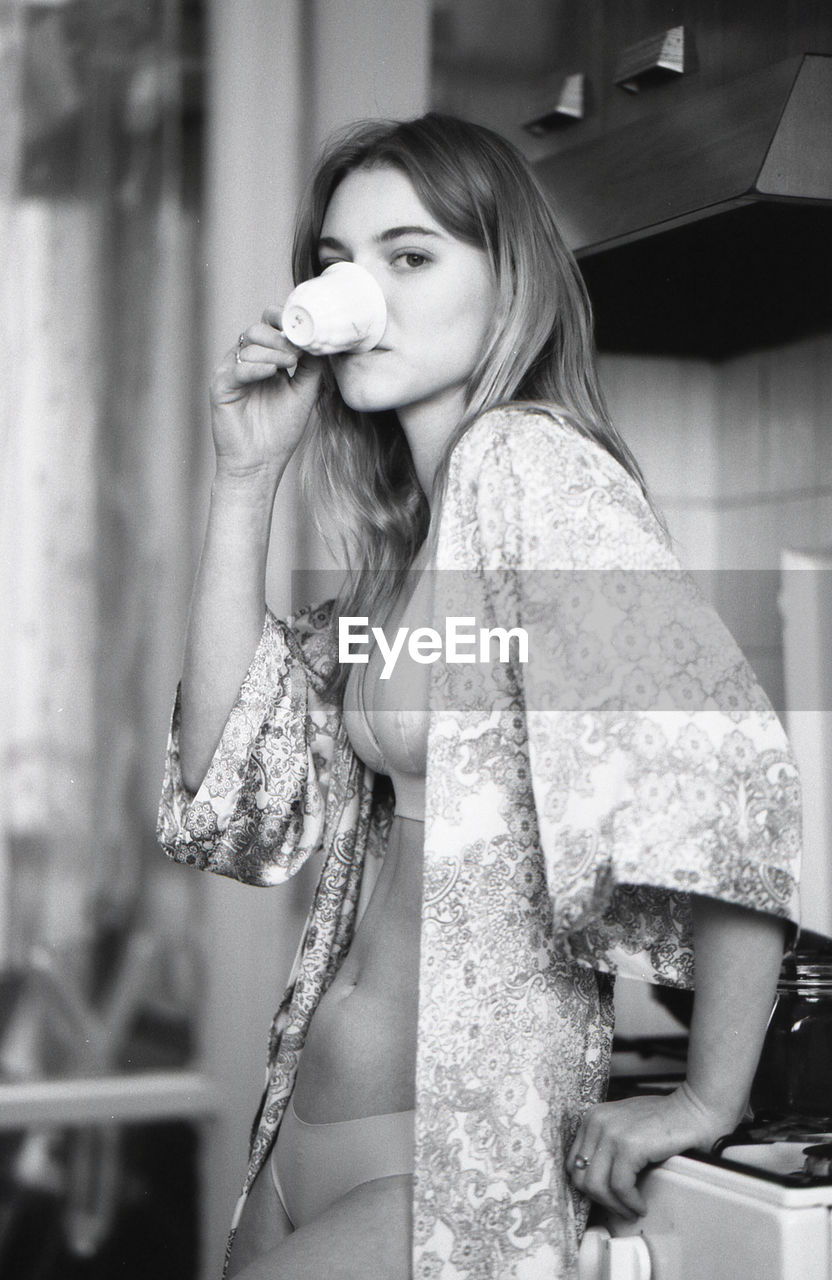 Portrait of sensuous young woman having coffee in kitchen at home