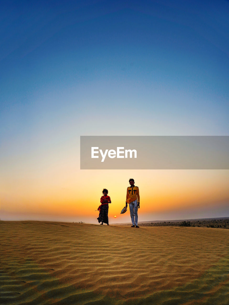 Portrait of people walking on sand against sky during sunset