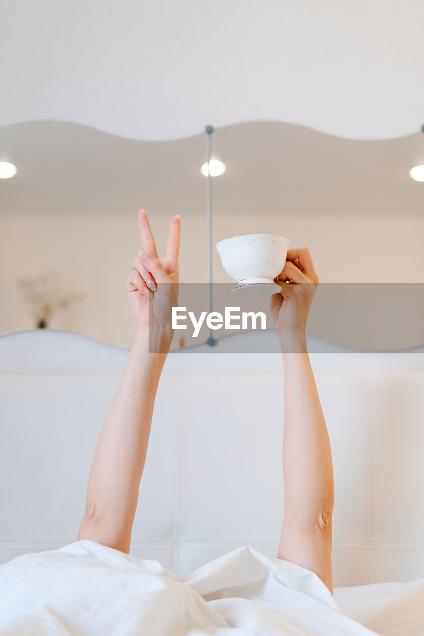 Young woman with a coffee mug in bed with white linens. minimal happy morning