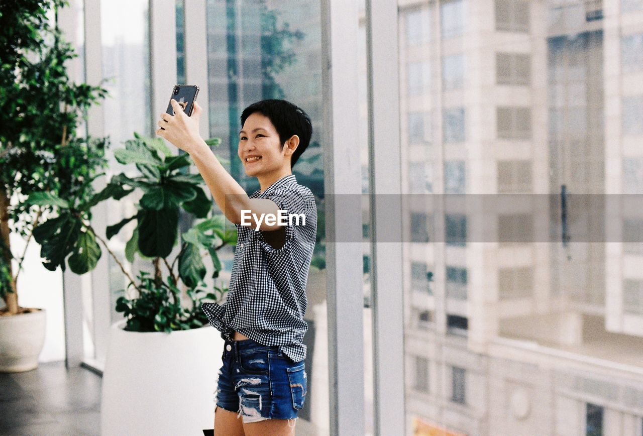 Woman taking selfie through mobile phone against window