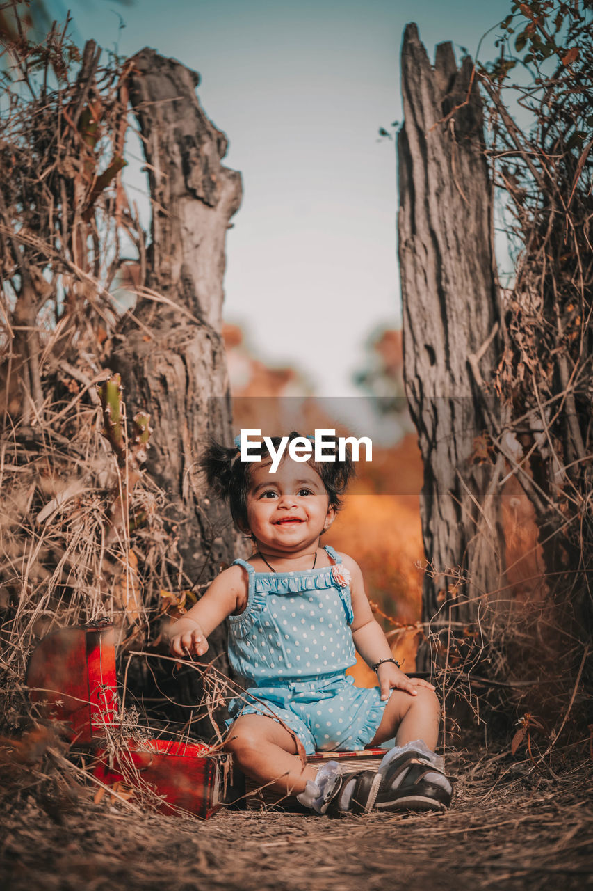 PORTRAIT OF HAPPY BABY SITTING ON TREE