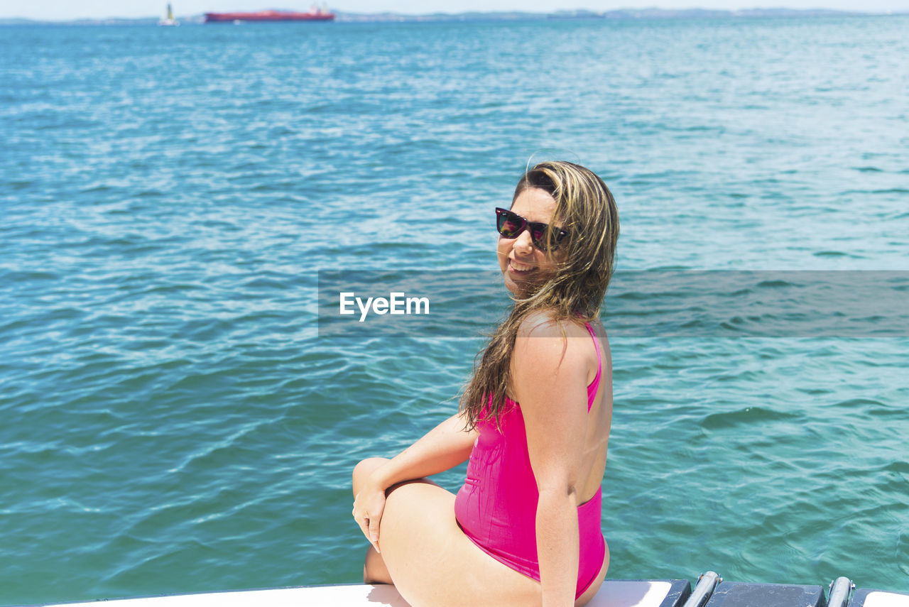 A woman on top of a boat against the sea in the background. 