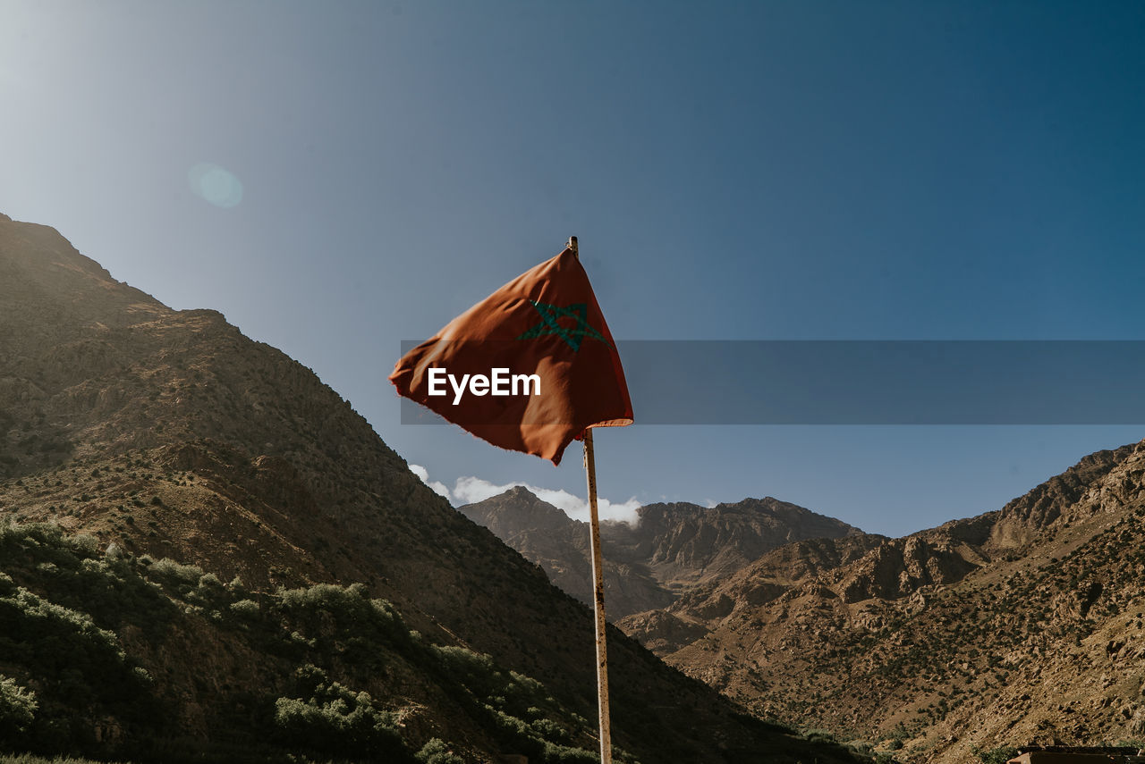 LOW ANGLE VIEW OF FLAG ON MOUNTAIN AGAINST SKY