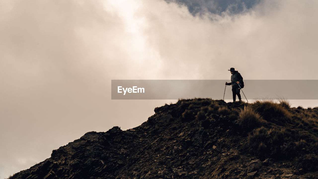 Low angle view of man hiking on mountain against cloudy sky