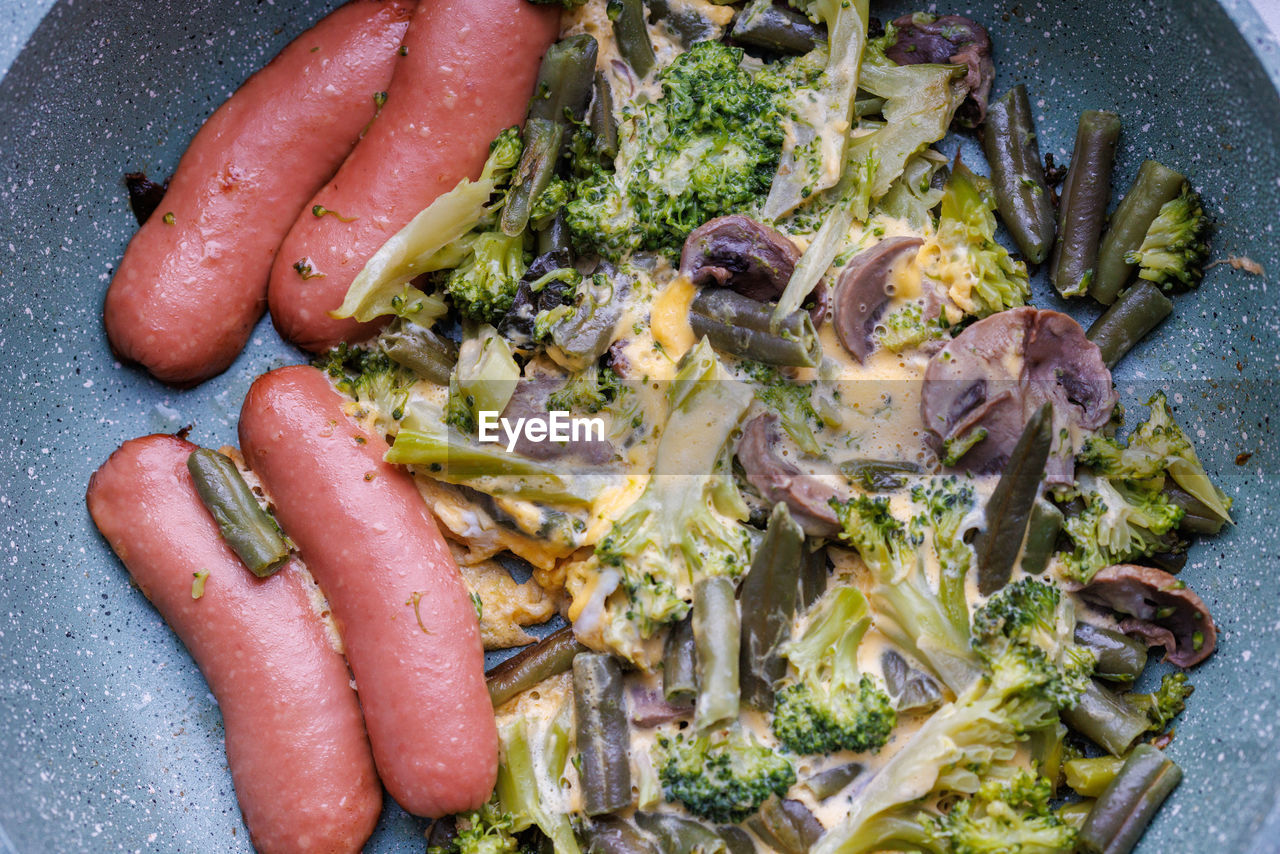 Fried sausages and vegetables with mushrooms and chicken egg on skillet