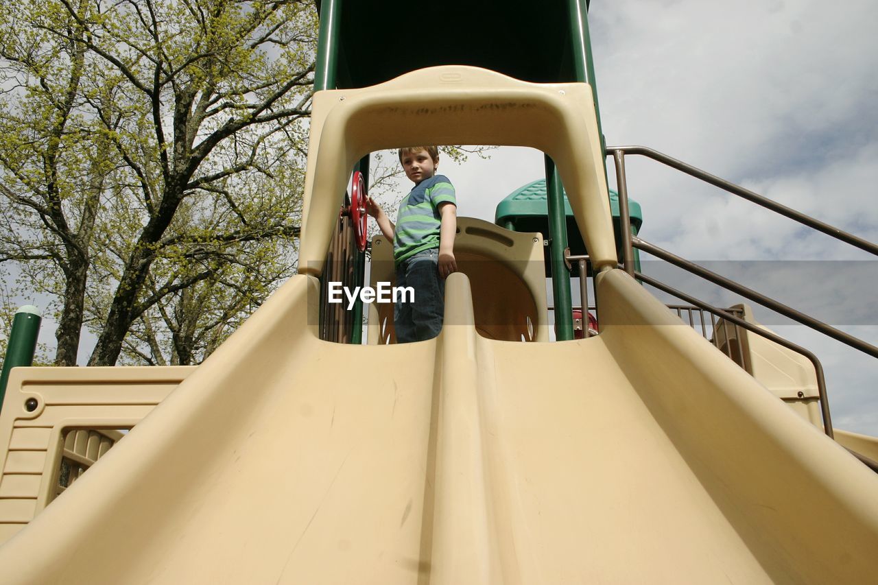 Low angle portrait of boy standing on slide at playground