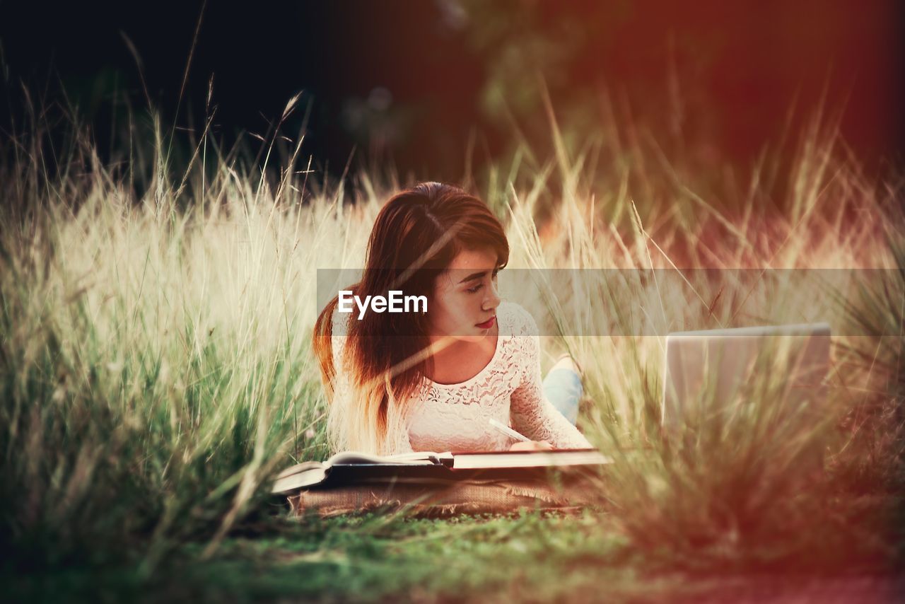 Young woman using laptop while lying on grassy field