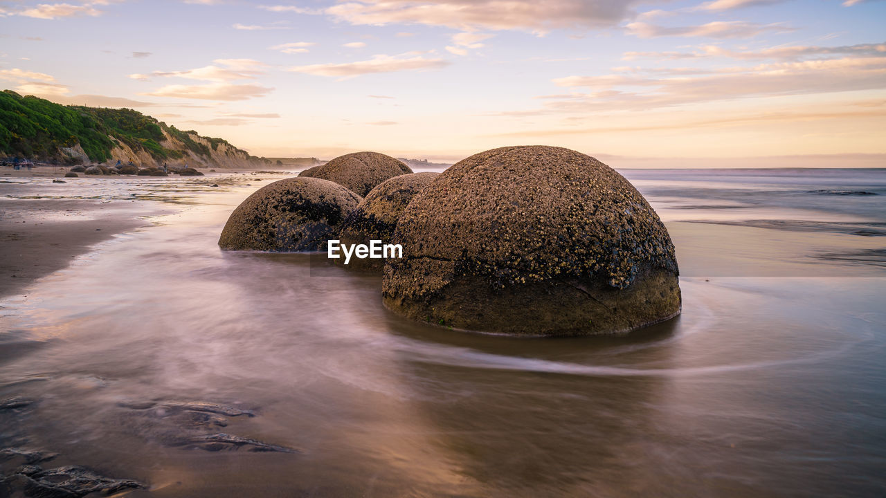 Scenic view of rocks on beach against sky during sunset