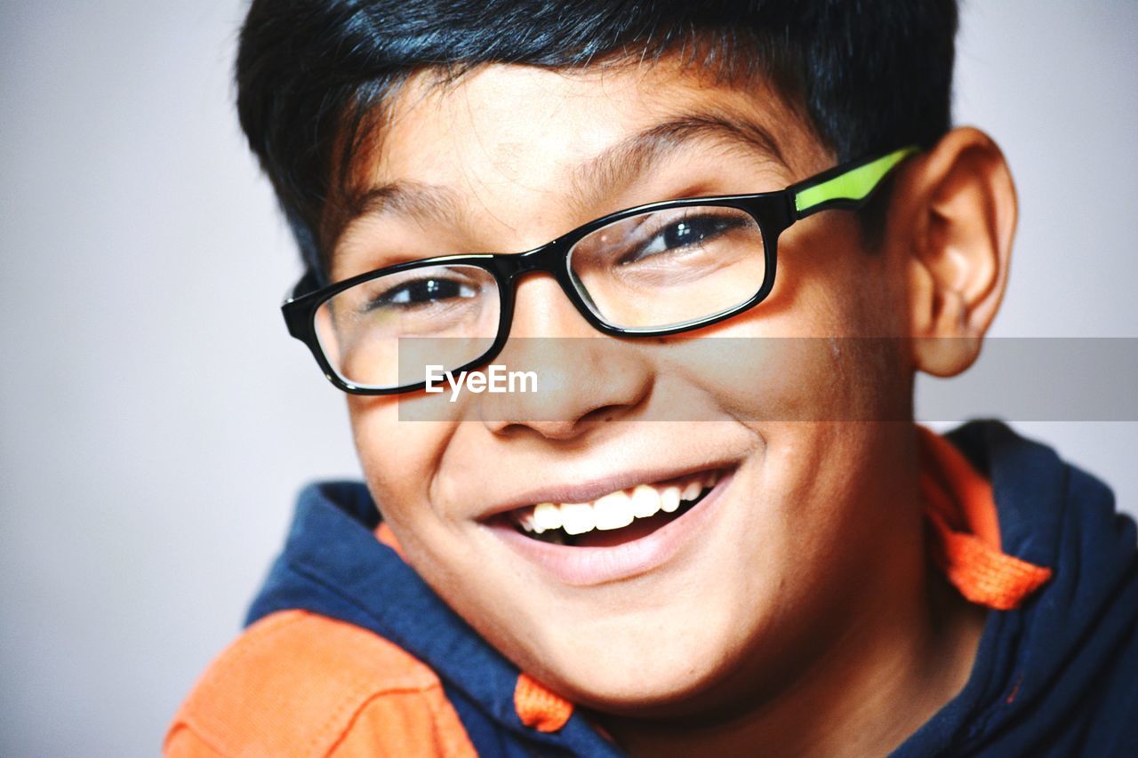 Close-up portrait of happy boy wearing eyeglasses against wall