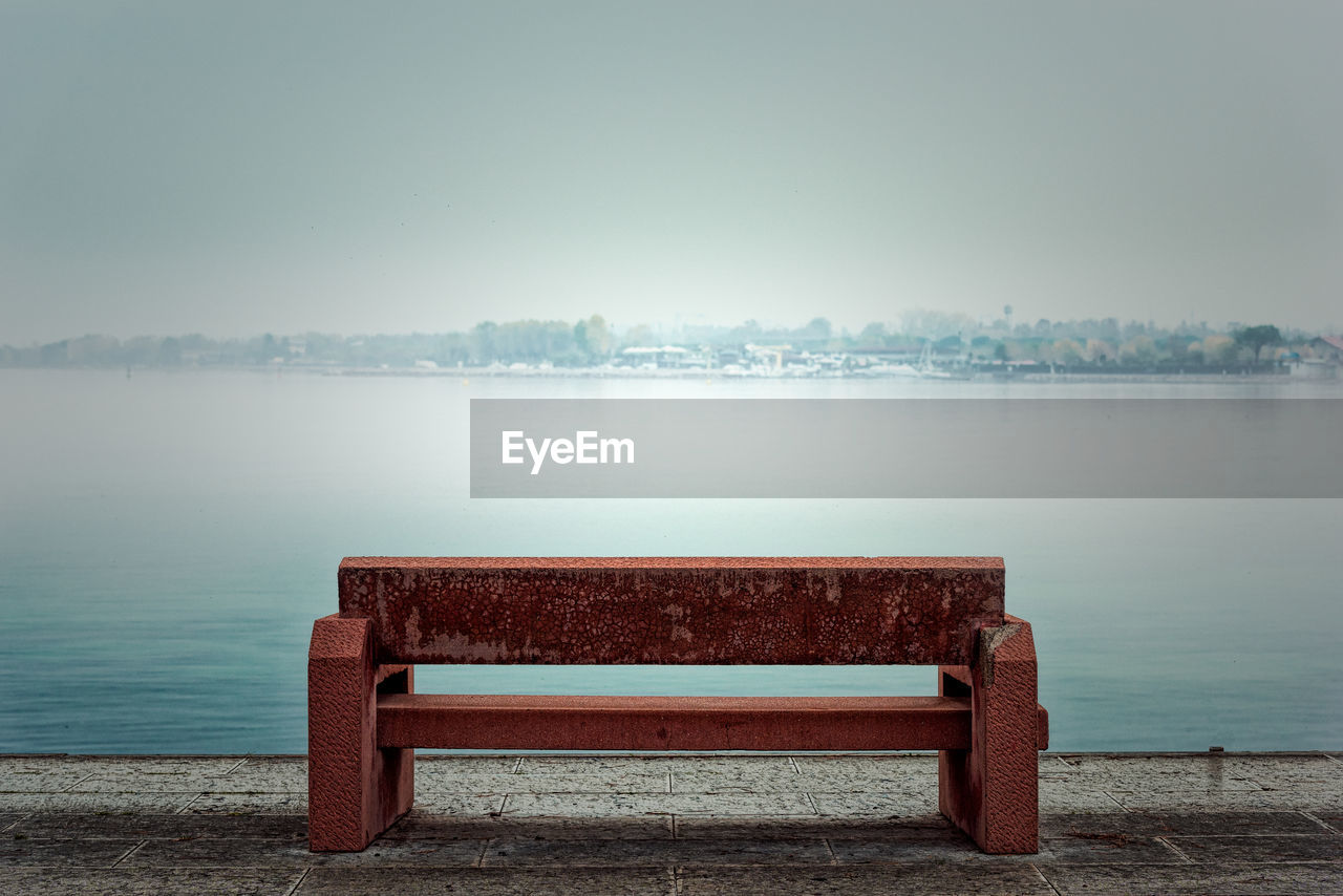 Empty bench by lake against clear sky