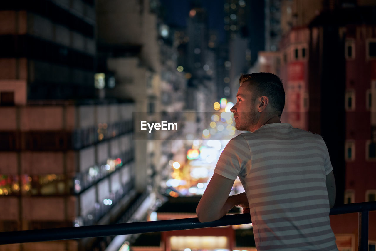 Rear view of man looking at illuminated city at night