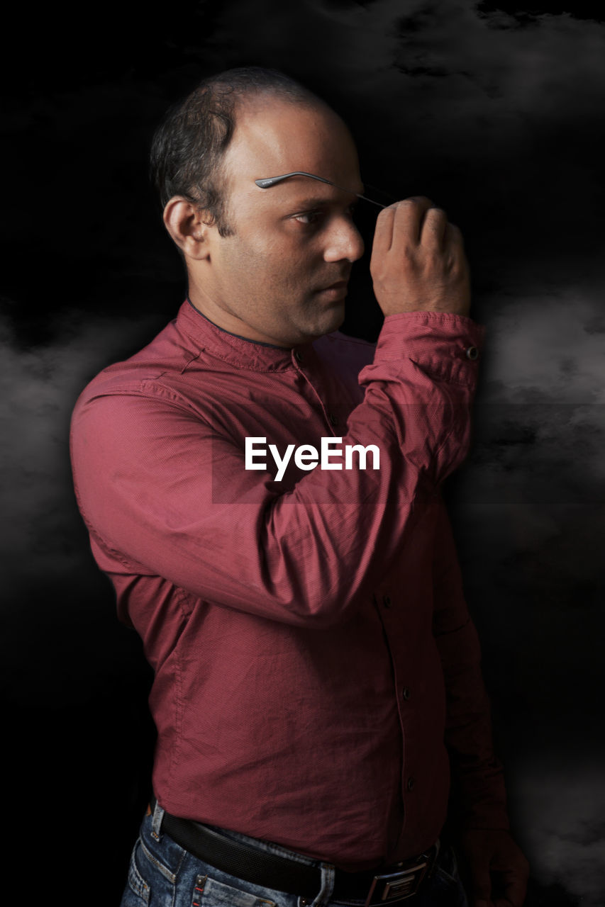 PORTRAIT OF YOUNG MAN STANDING OVER BLACK BACKGROUND