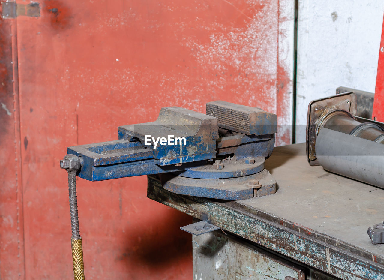 Old blue iron vise on workbench workshop in blurred environment of other equipment and tools,
