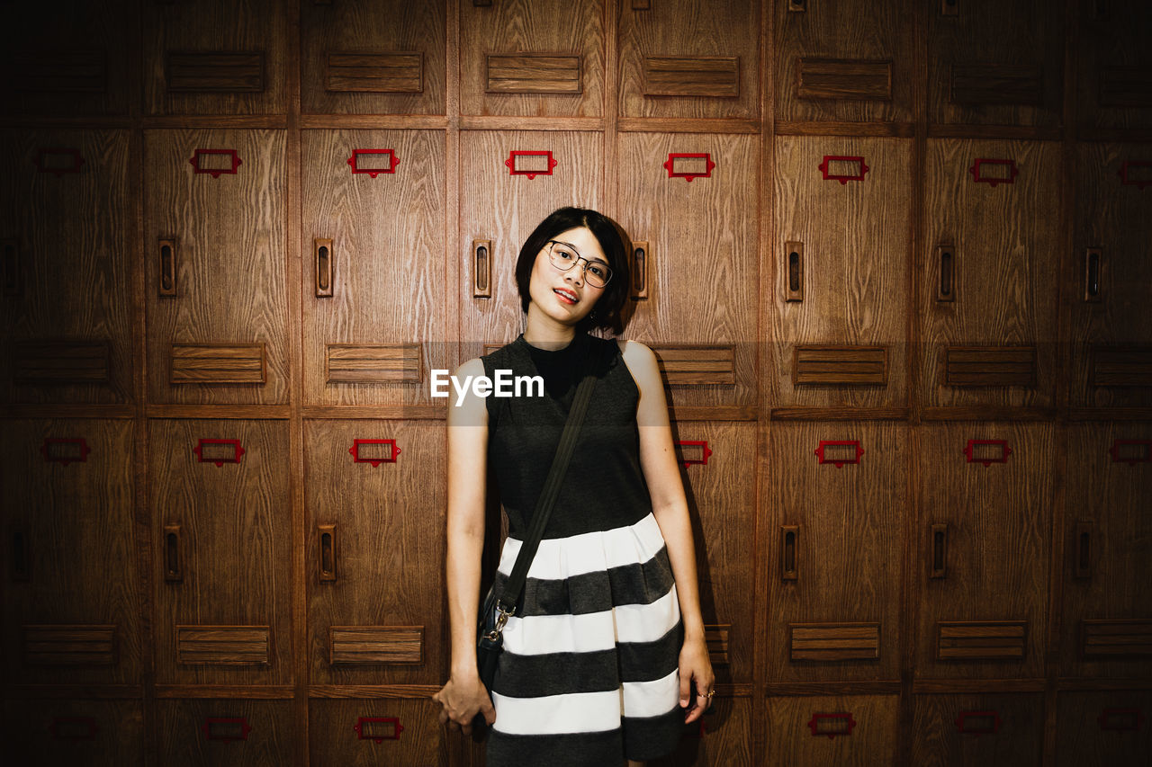 Portrait of young woman standing against lockers