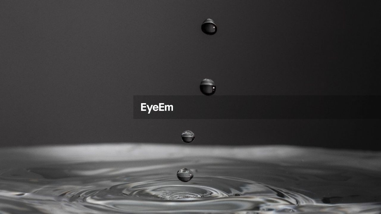 Close-up of drop falling on water against black background