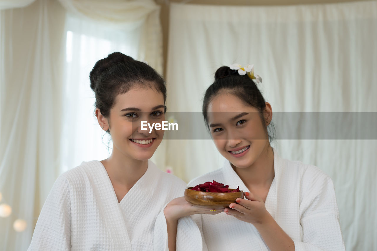 Smiling young women in bathrobes sitting in spa