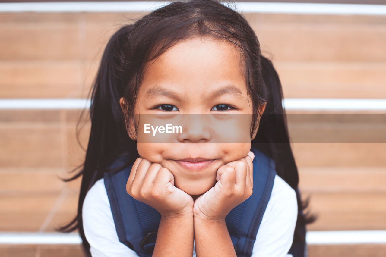 Close-up portrait of cute smiling girl with hands on chin