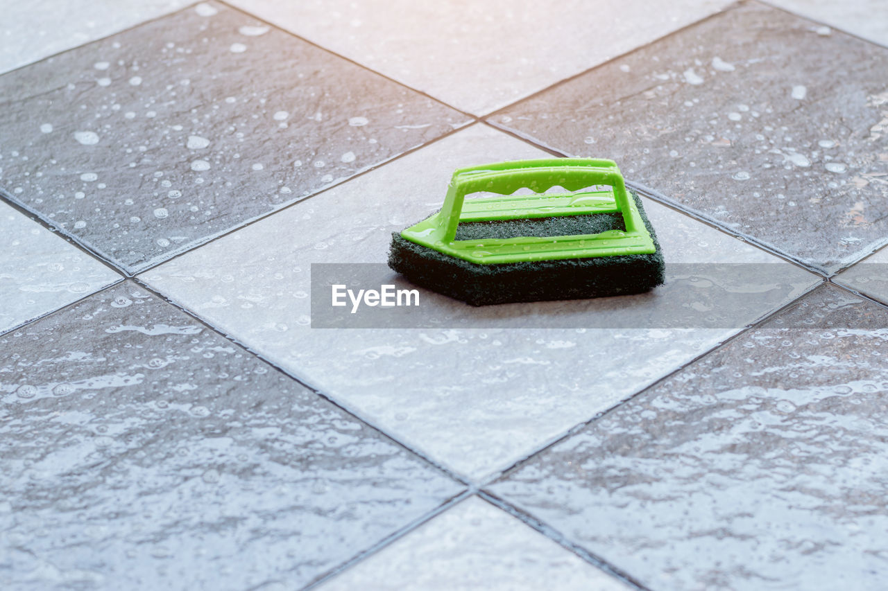 Close up a green plastic brush for scrubbing and cleaning floors placed on a wet tiled floor.