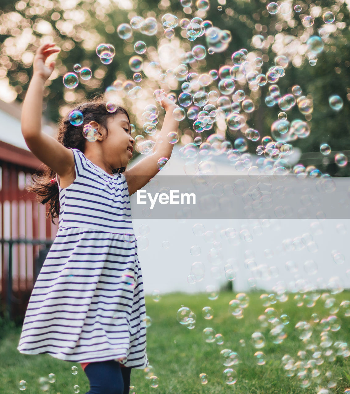 Diverse mixed race pre school girl outdoors during summer having fun in backyard with bubbles 