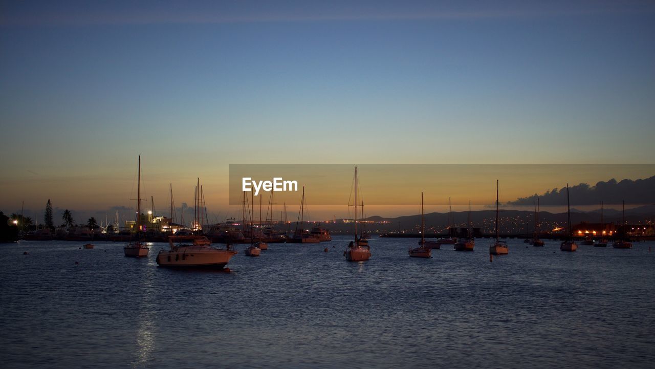 Sailboats moored on river against sky during sunset