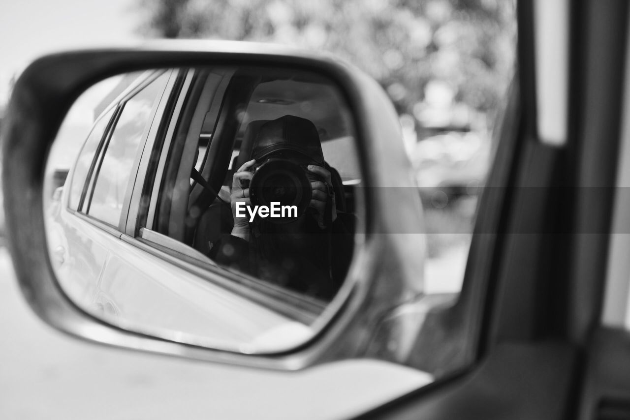 Reflection of person photographing on side-view mirror of car