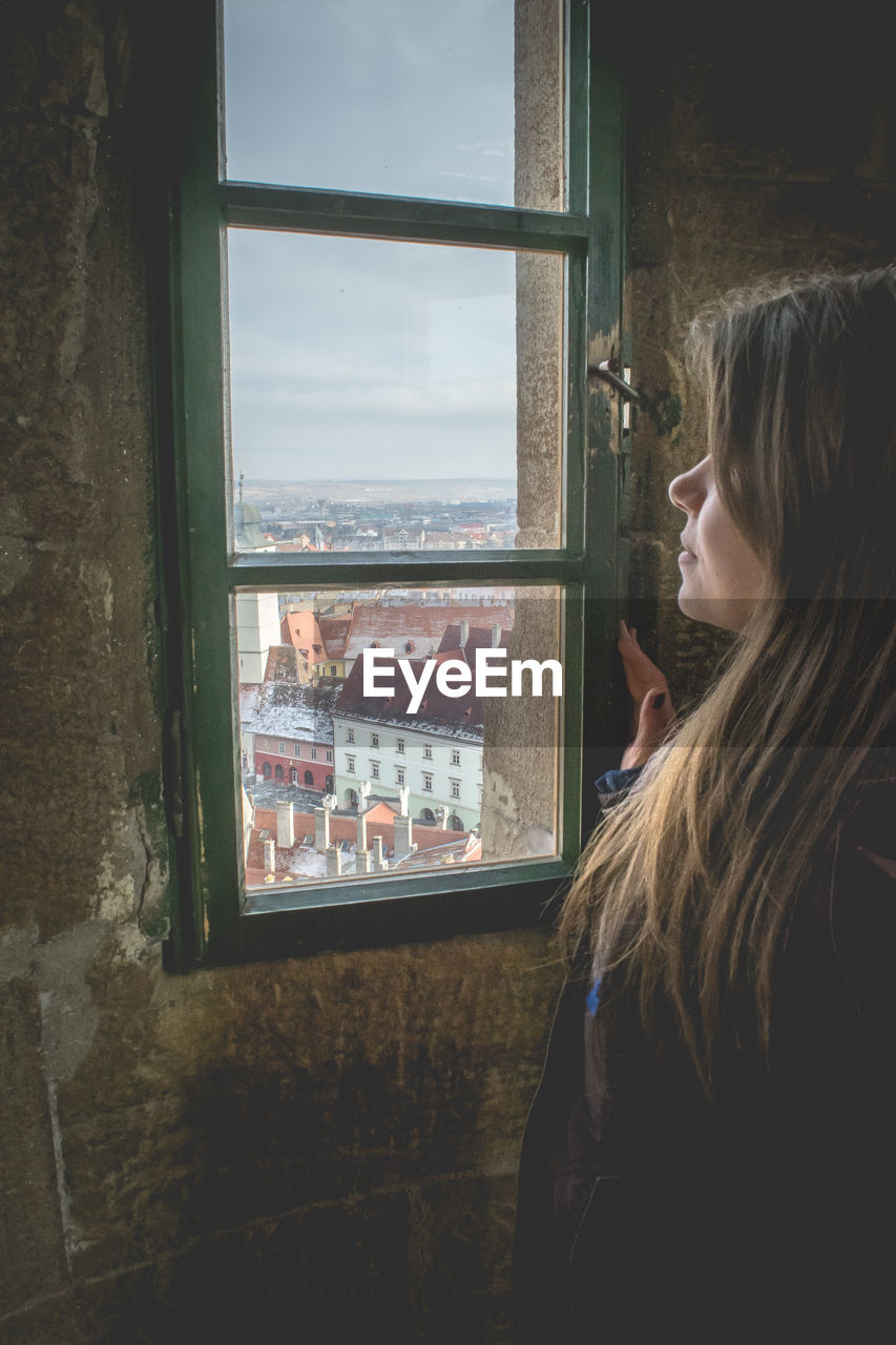 Side view of woman looking through window