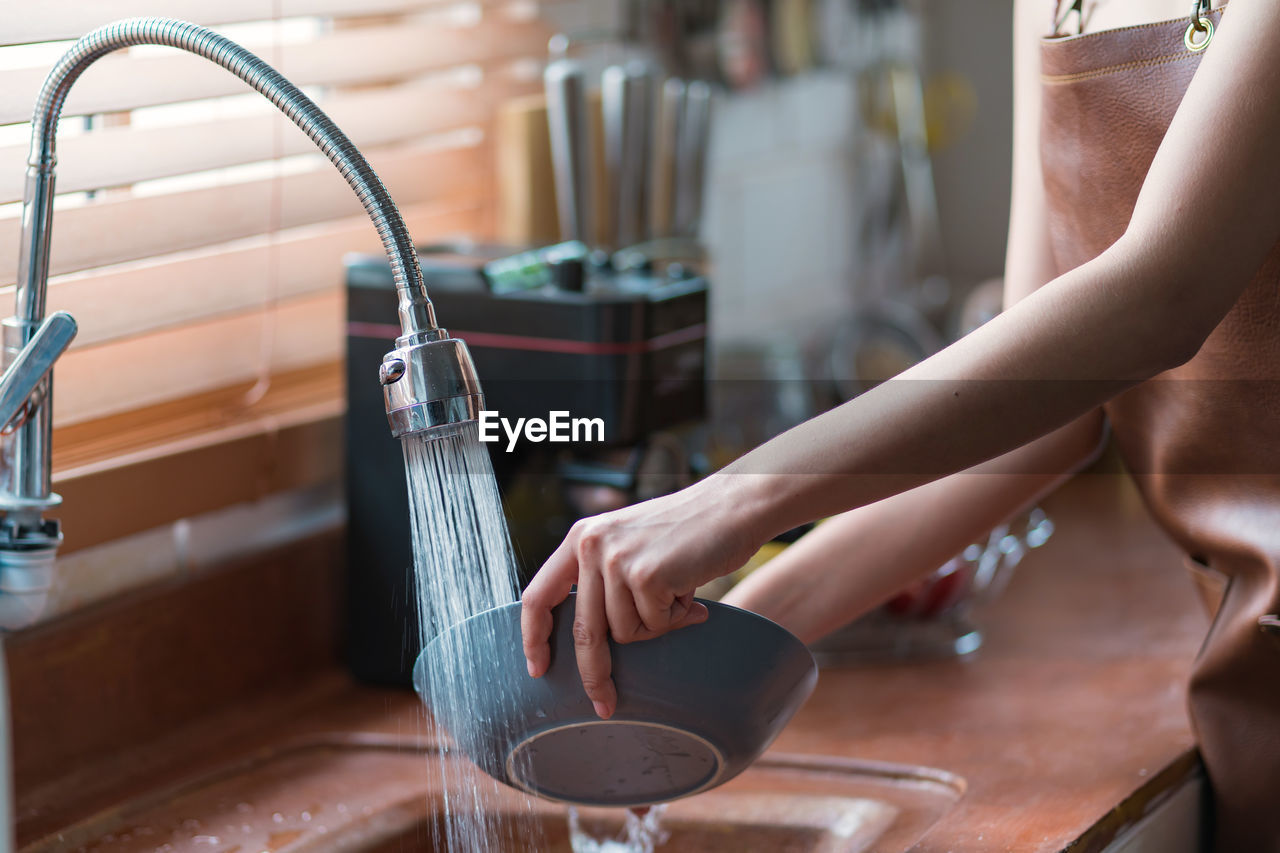 Attractive young woman or housewife washing dishes in the kitchen sink at home.