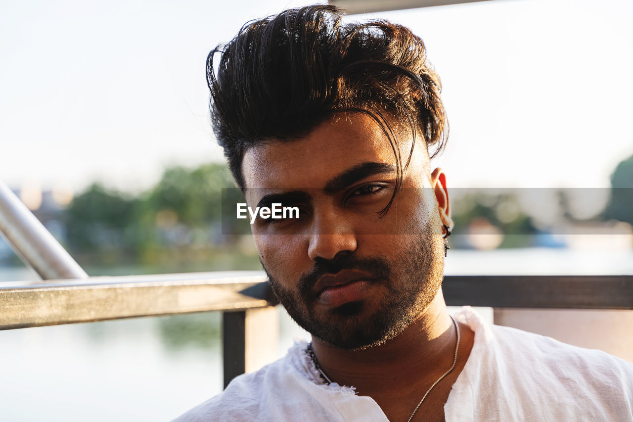 Portrait of young handsome pakistani man sitting on boat sailing during summer vacation on a river