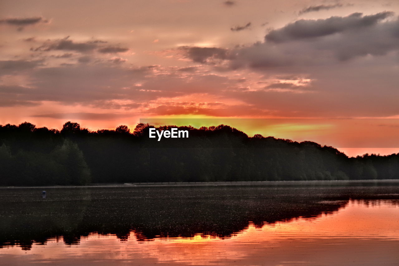 SCENIC VIEW OF LAKE BY SILHOUETTE TREES AGAINST ORANGE SKY