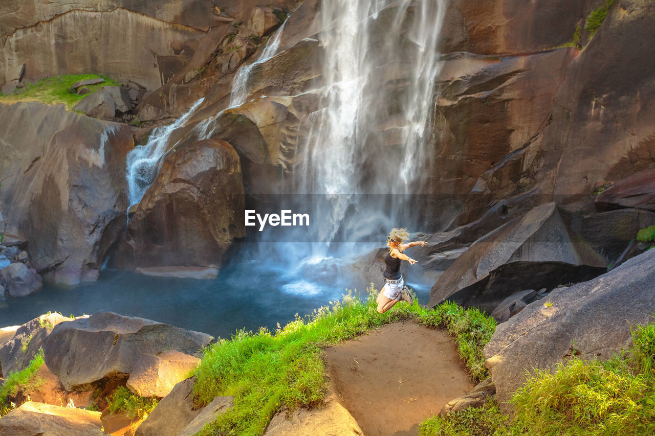 High angle view of woman jumping against waterfall