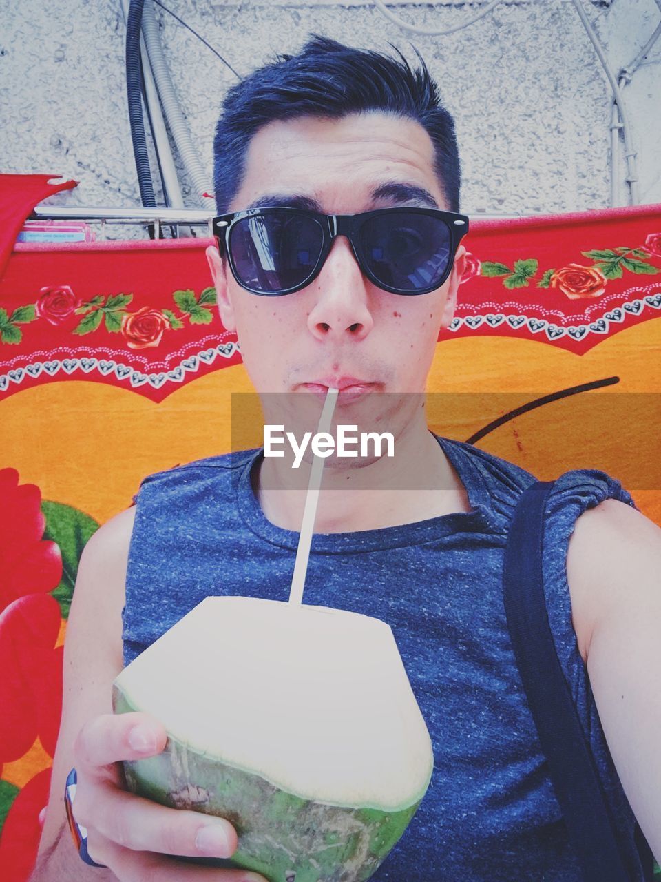 Portrait of man in sunglasses drinking coconut water against fabric