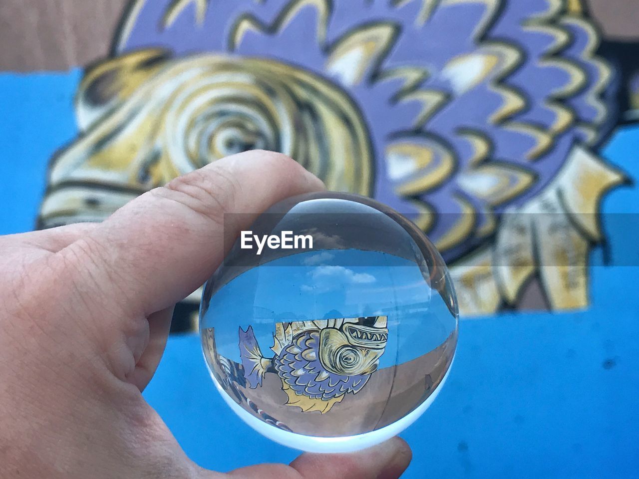 Cropped hand holding crystal ball with reflection of mural on wall