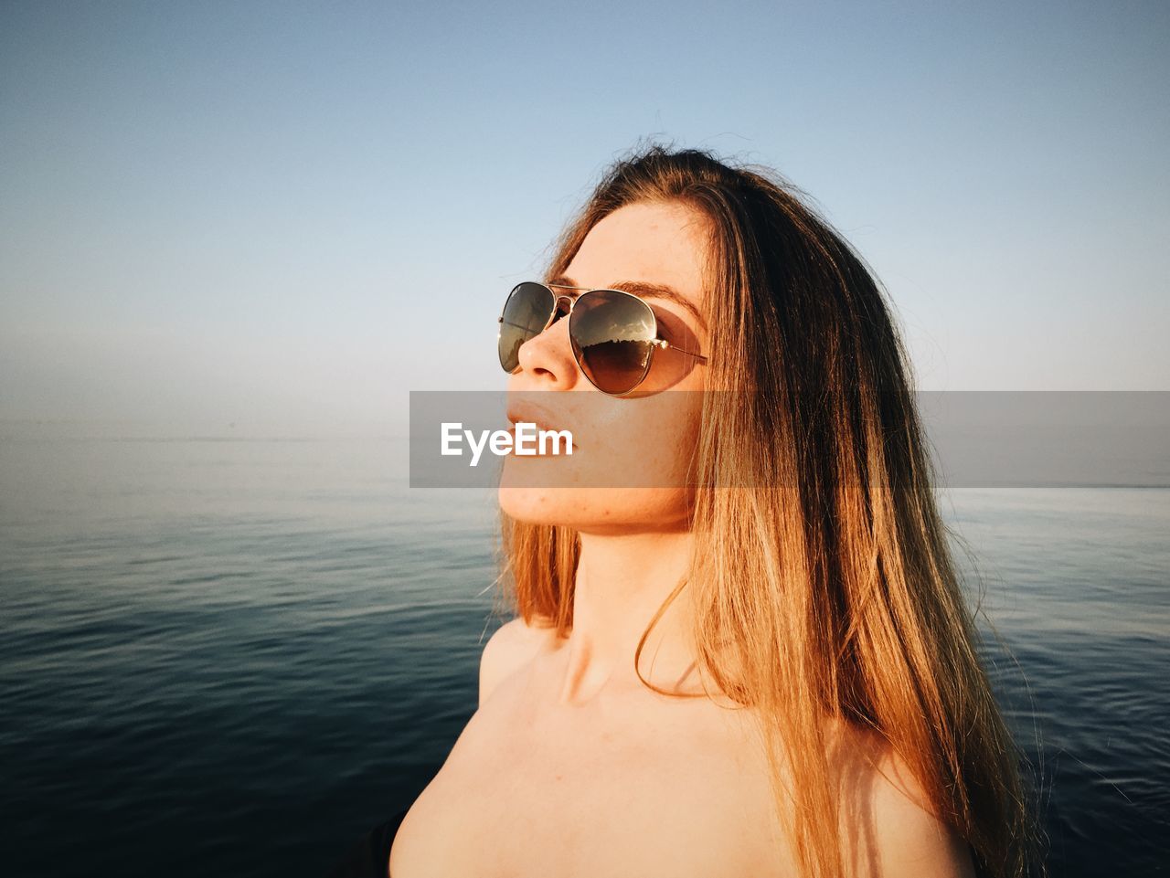 Close-up of young woman wearing sunglasses at sea against clear sky