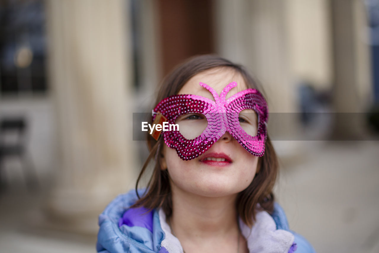 Close-up of small girl with bright eyes wearing a shiny butterfly mask