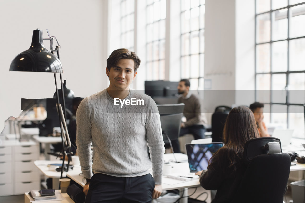 Portrait of male entrepreneur leaning on desk in office