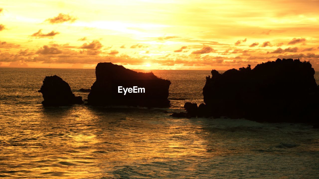 SCENIC VIEW OF ROCK FORMATION IN SEA AGAINST SKY DURING SUNSET