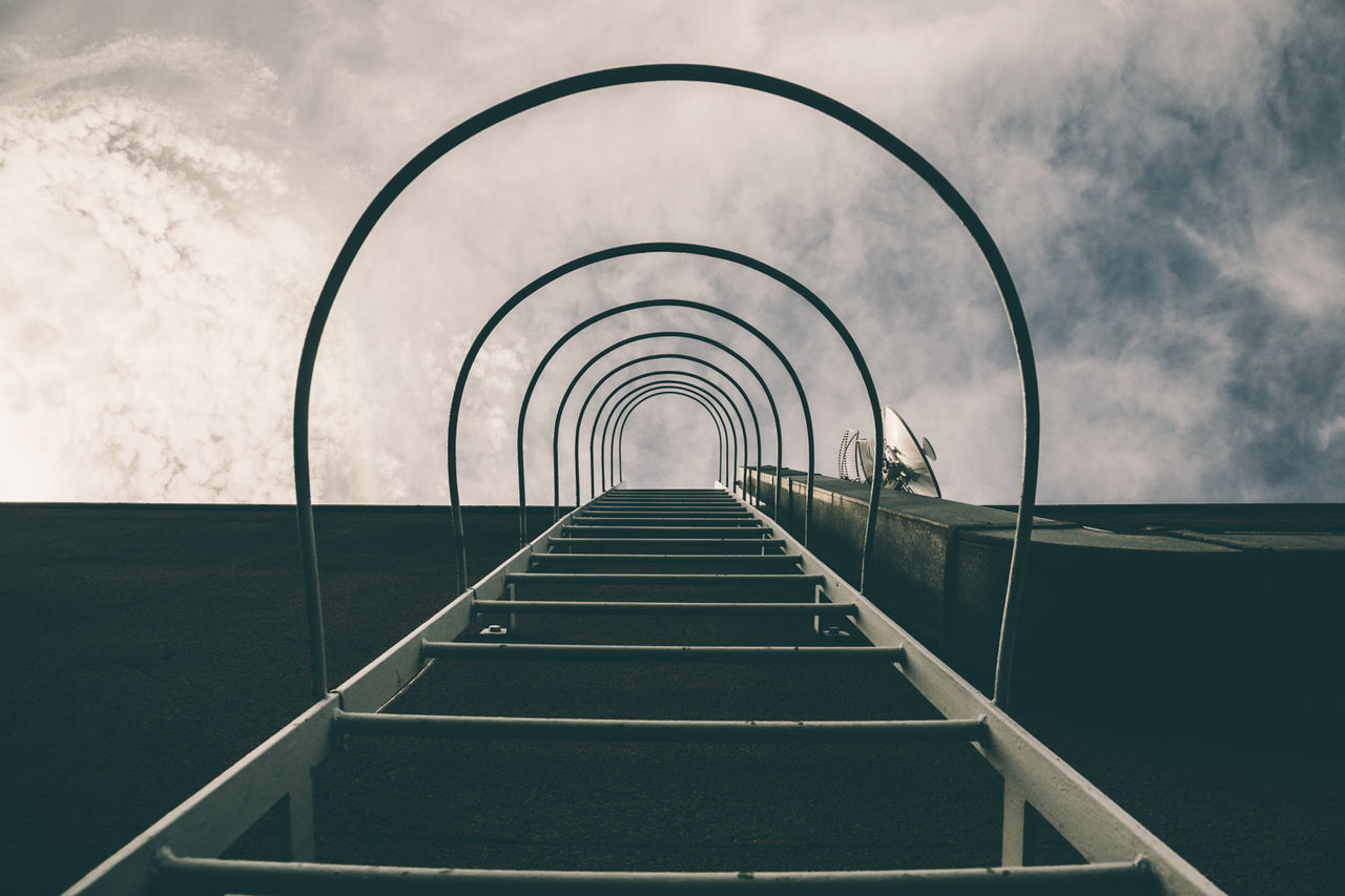 Directly below shot of ladder against cloudy sky