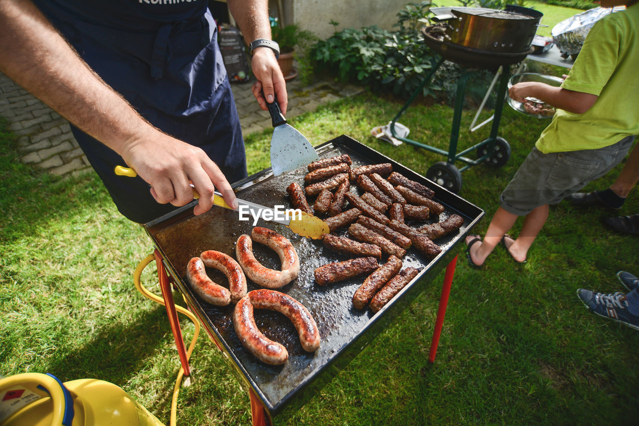 High angle view of men preparing sausages on barbecue grill in yard