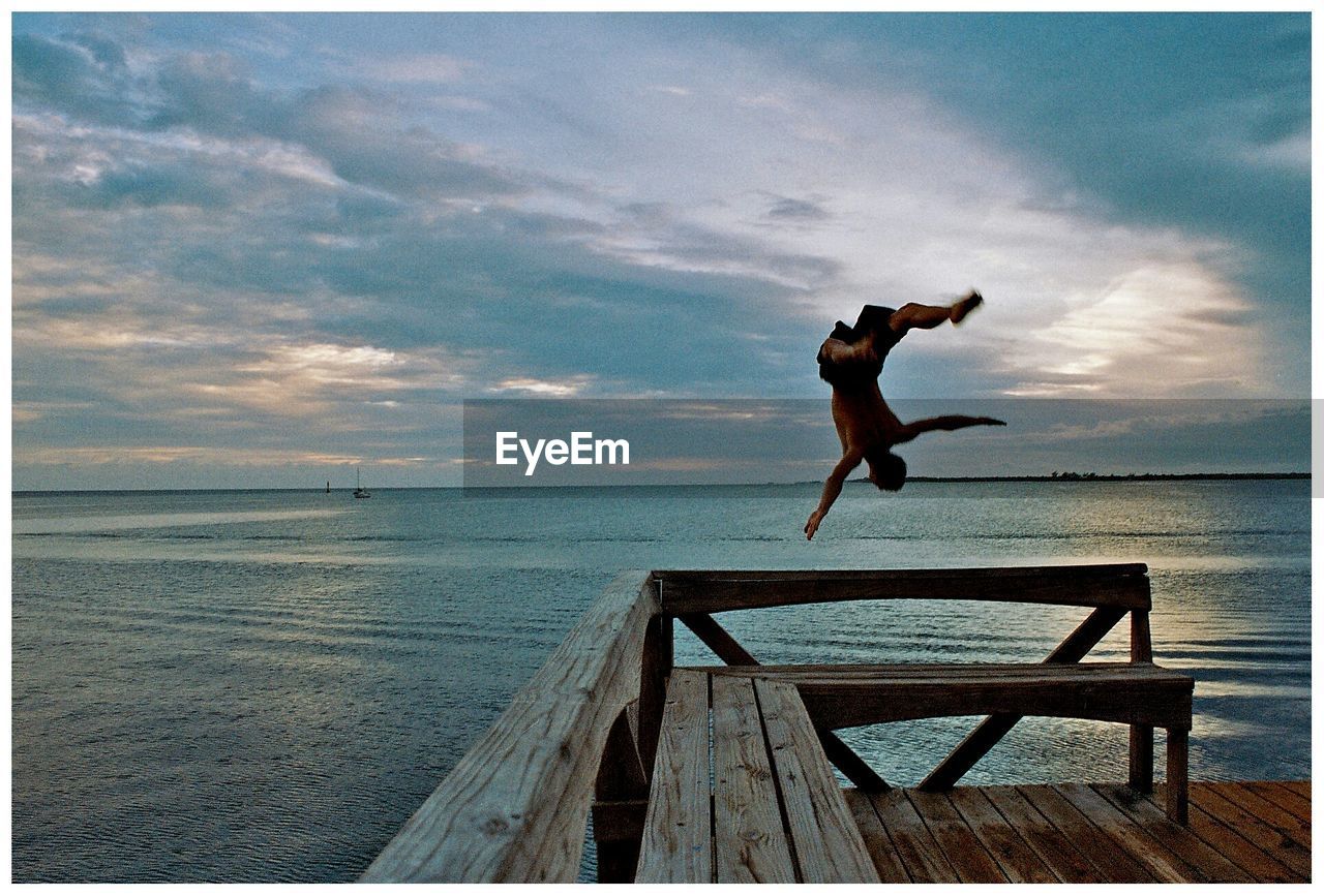 View of man back flipping from pier into sea