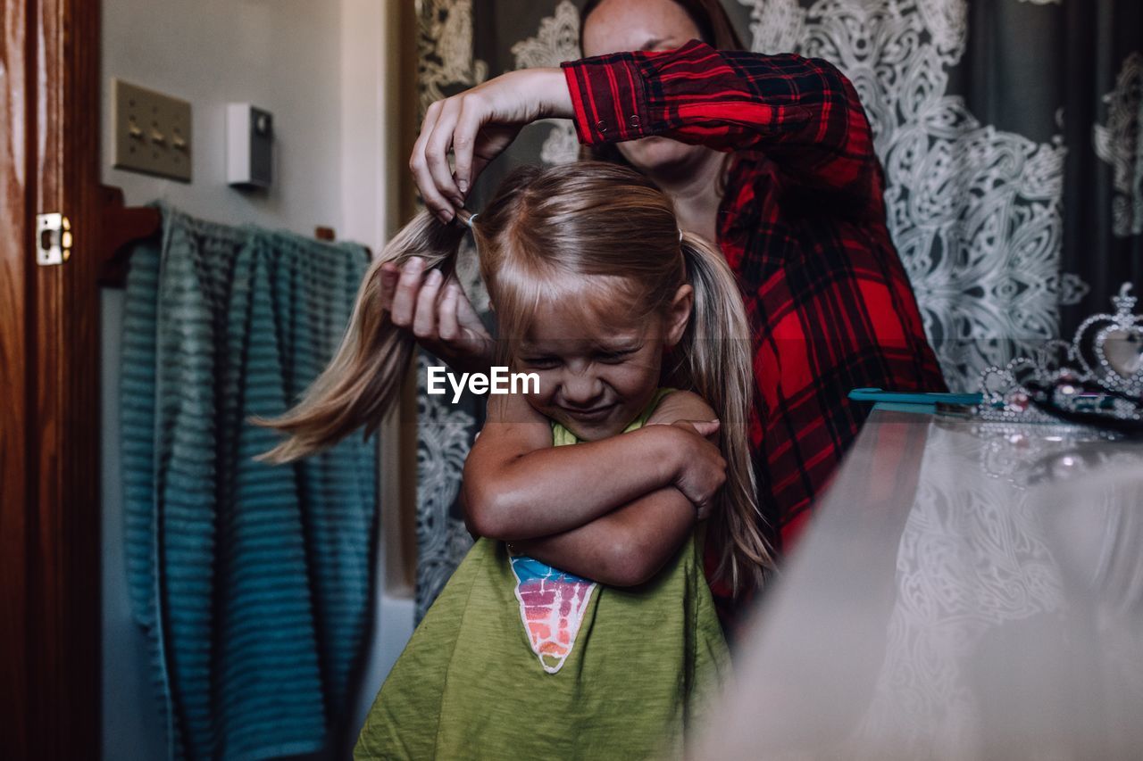 Mother combing hair of daughter at home