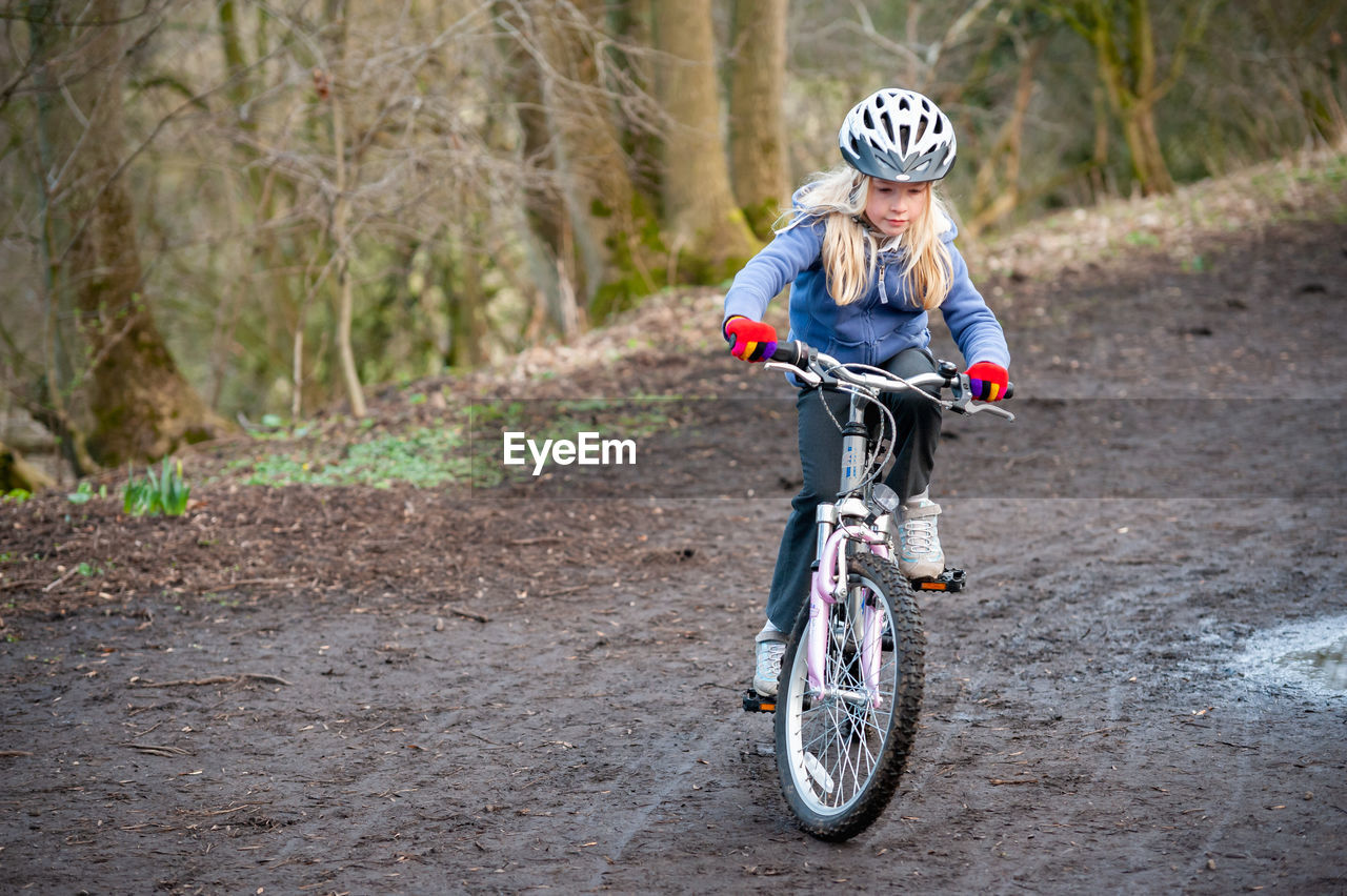 Girl riding bicycle on dirt road in forest